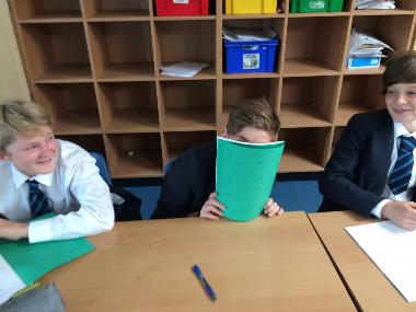 a student hiding behind a green notebook sitting at a table